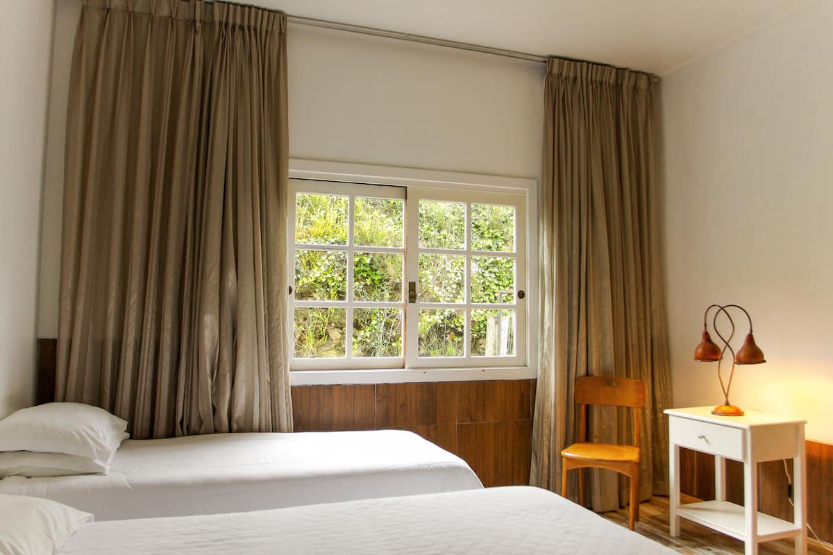 Un dormitorio con dos camas, una silla de madera, un escritorio y una ventana con cortinas.