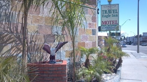 A brick building with a sign for Travel Eagle Inn Motel, featuring amenities like free internet, phones, and a refrigerator. - Travel Eagle Inn Motel (Long Beach)