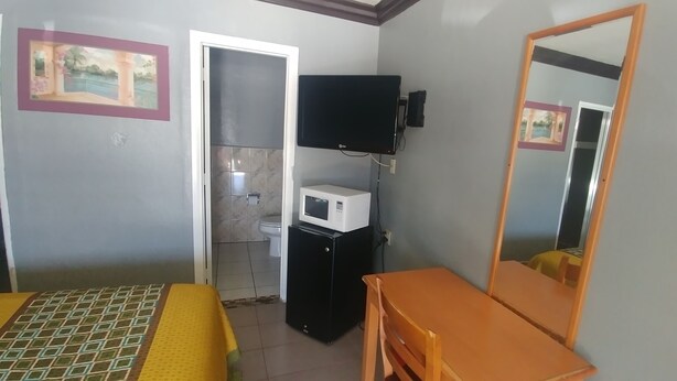 A small room with a bed, a wooden table, a mirror, a TV, and a microwave. - Travel Eagle Inn Motel (Long Beach)