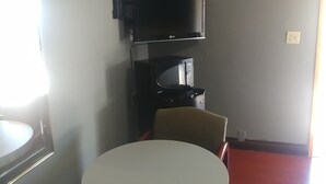 A small room with a round table and two chairs, a television mounted on the wall, and a window providing natural light. - Travel Eagle Inn Motel (Long Beach)