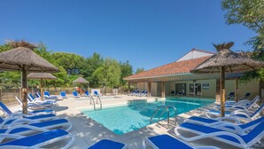 A pool area with blue and white lounge chairs, a swimming pool, and thatched umbrellas. - Résidence Odalys Le Petit Pont (Hourtin)