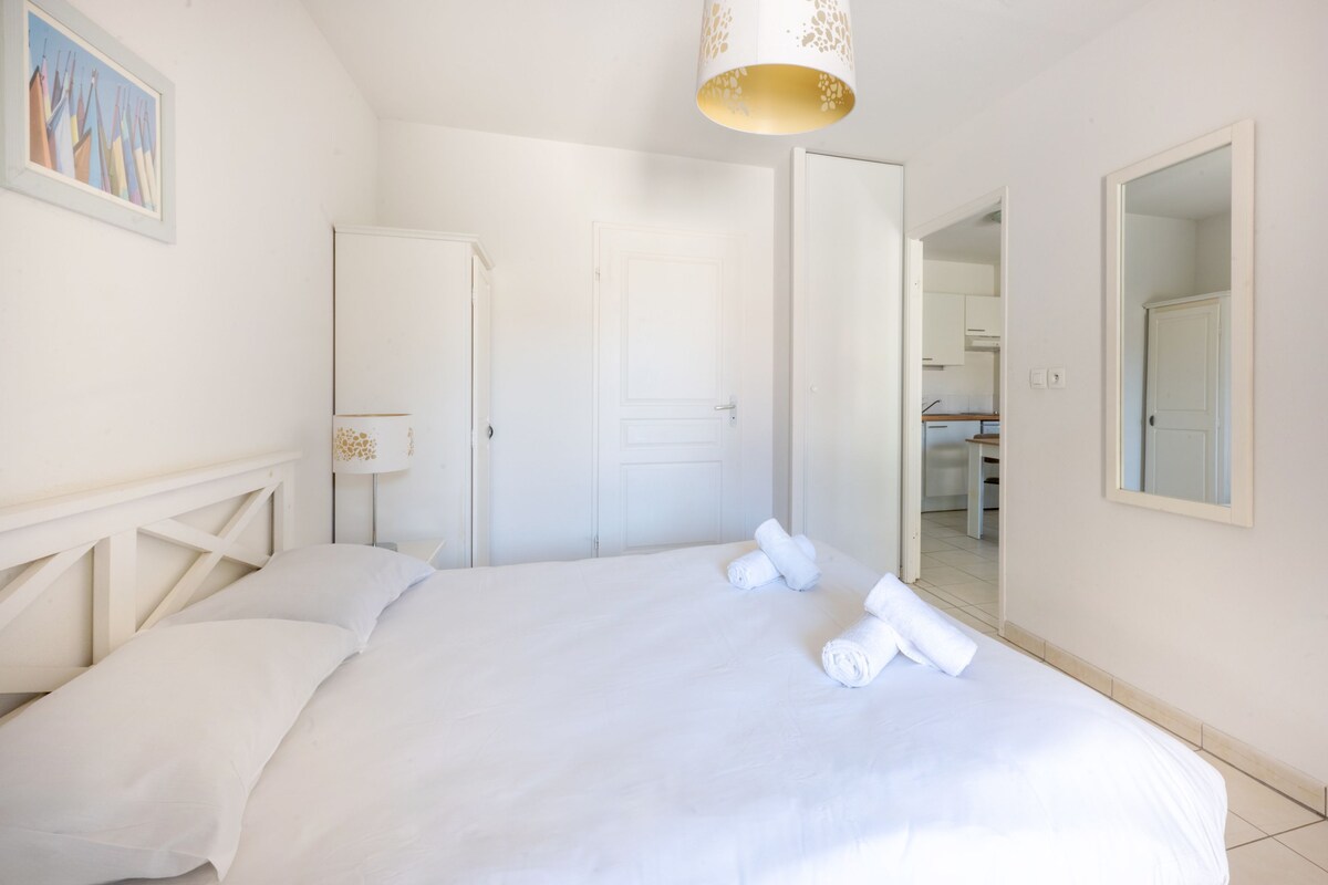 Un dormitorio con cama, una puerta, un espejo y un pasillo que da a una cocina.