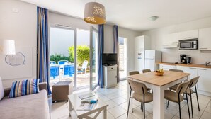 A modern kitchen with white cabinets, a microwave, and a coffee maker. There is a dining table with chairs and a sofa with striped cushions. - Résidence Odalys Le Petit Pont (Hourtin)