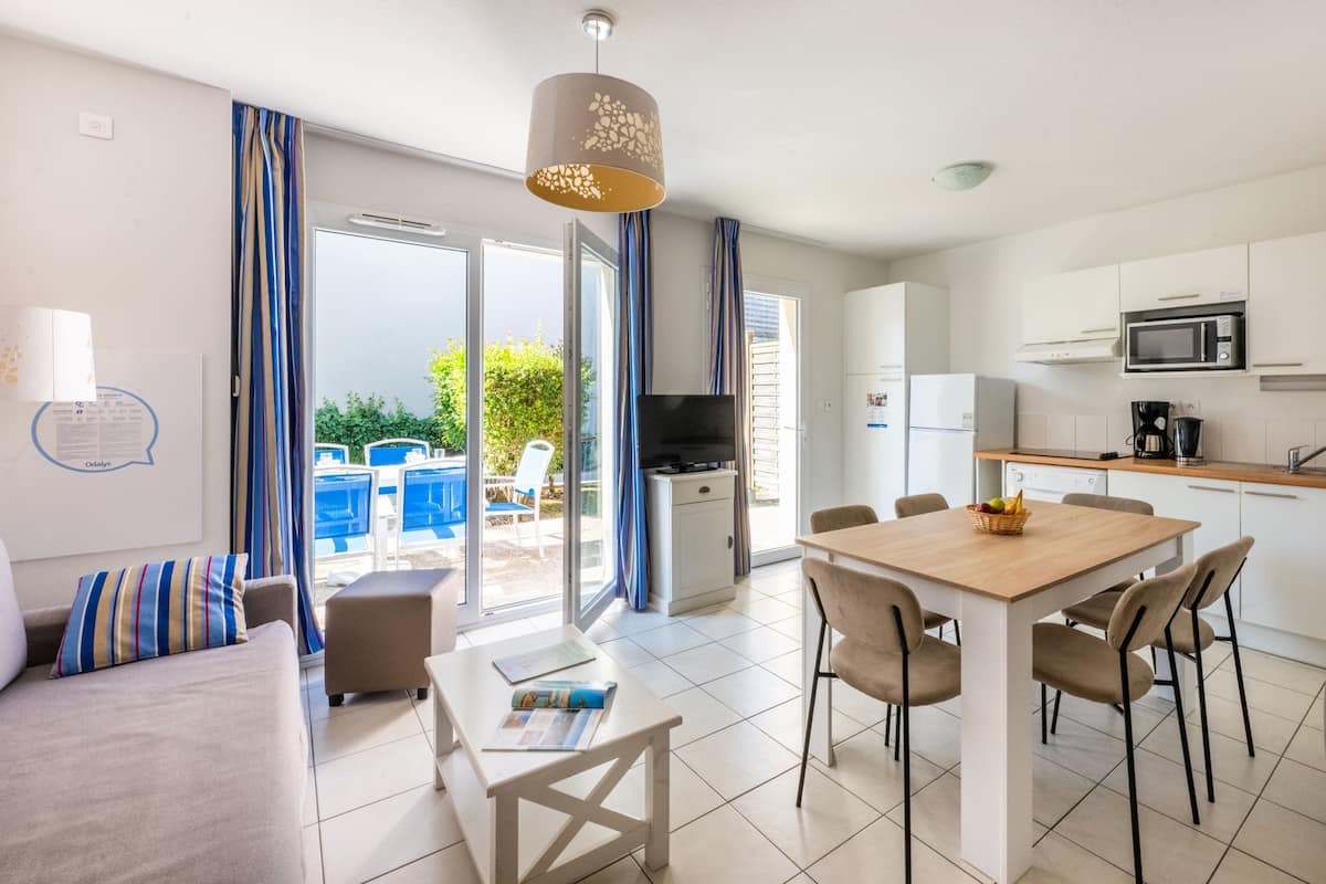 A modern kitchen with white cabinets, a microwave, and a coffee maker. There is a dining table with chairs and a sofa with striped cushions.