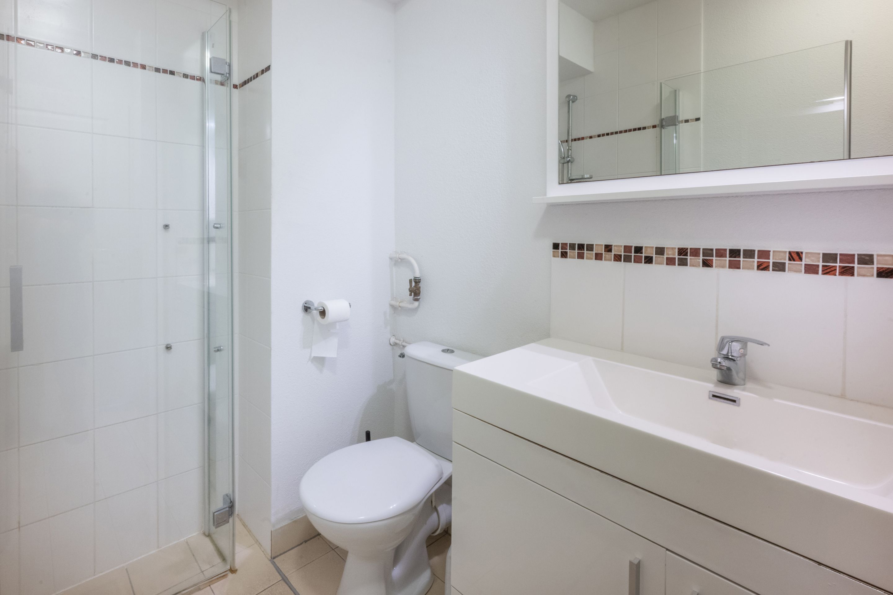 A bathroom with a glass shower enclosure, a toilet, a sink with a mirror above, and a tiled backsplash.