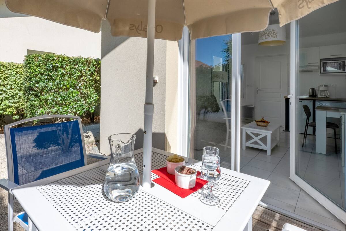 An outdoor dining area with a table set for two, a pitcher, glasses, and a bowl of fruit.