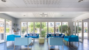 A spacious lobby with modern blue and light blue seating, large windows, and a view of the outside. - Résidence Odalys Le Petit Pont (Hourtin)