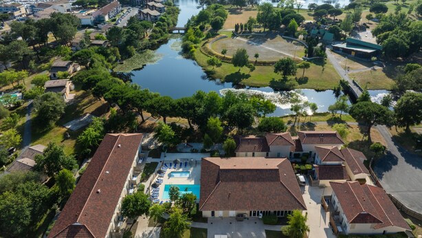 An aerial view of a residential area with houses, a swimming pool, and a lake. - Résidence Odalys Le Petit Pont (Hourtin)