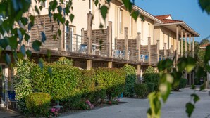 A hotel with a covered outdoor area, wooden deck, and lush greenery. - Résidence Odalys Le Petit Pont (Hourtin)