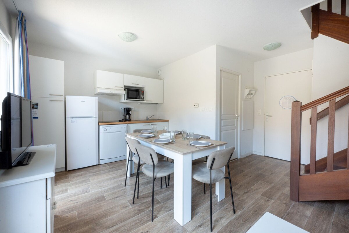 Una cocina moderna con armarios blancos, un microondas y una mesa de comedor preparada para cuatro comensales.