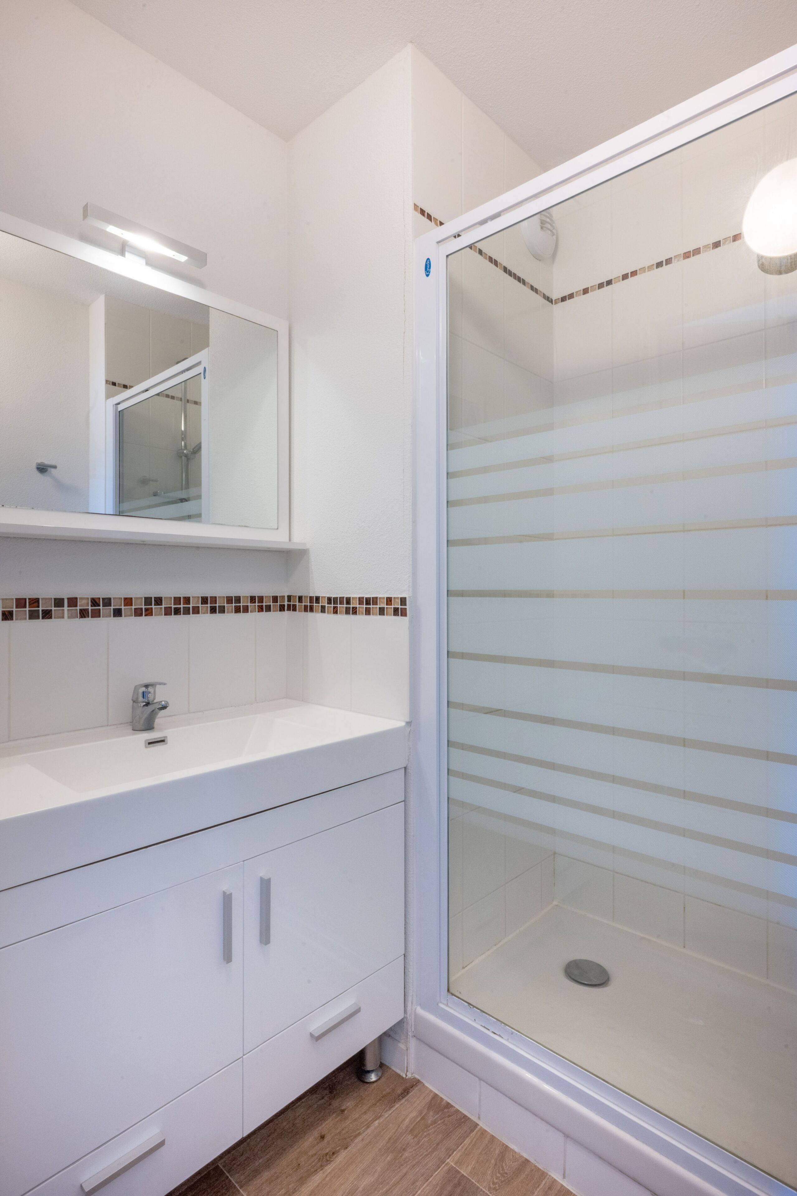 A modern bathroom with a white vanity, a glass shower enclosure, and a tiled backsplash.