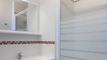 A modern bathroom with a white vanity, a glass shower enclosure, and a tiled backsplash.