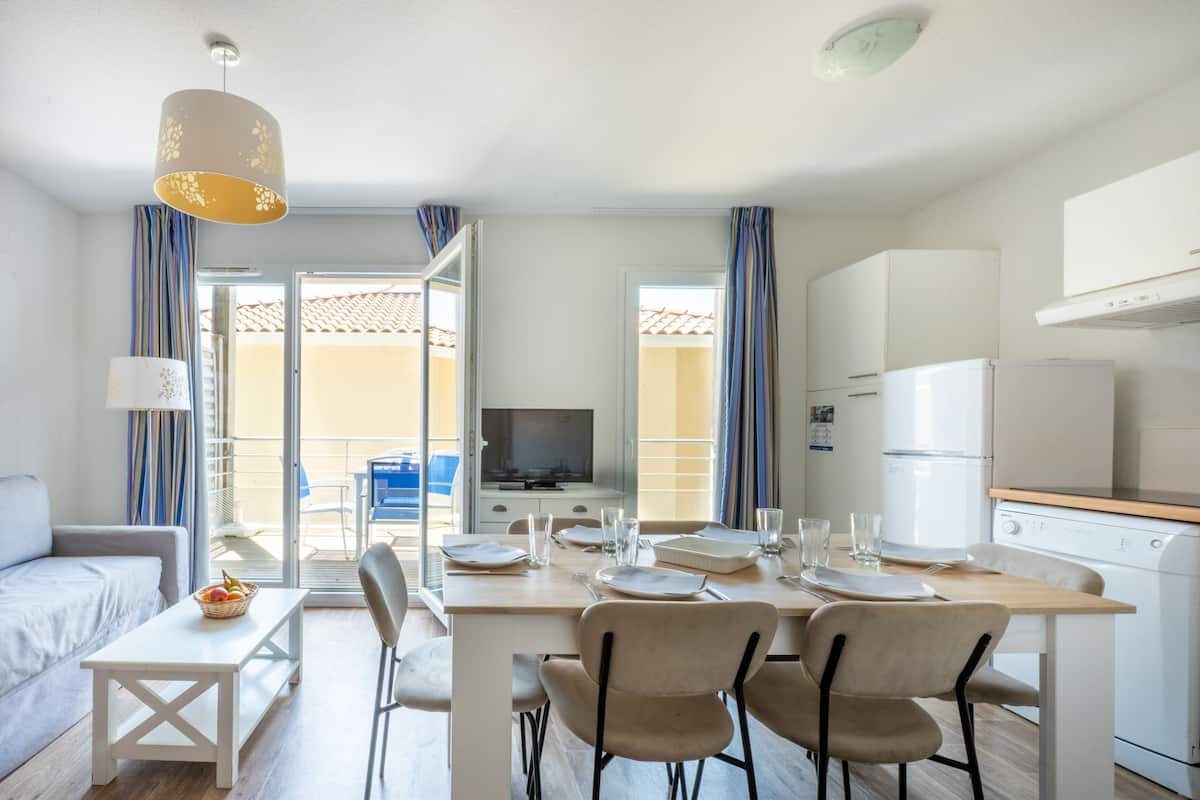 A modern kitchen with a dining area, a TV, and a balcony with a view.