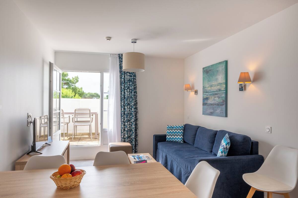 Ein modernes Wohnzimmer mit einer Couch, einem Esstisch mit Stühlen, einer Obstschale und Blick ins Freie.
