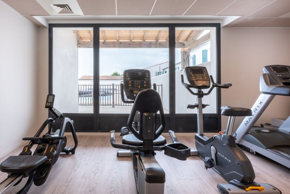 A gym with cardio machines, a rowing machine, and a view of buildings through large windows.