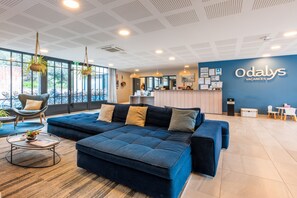 Un moderno vestíbulo de hotel con un amplio sofá azul, una mesa redonda de centro y un mostrador de recepción.