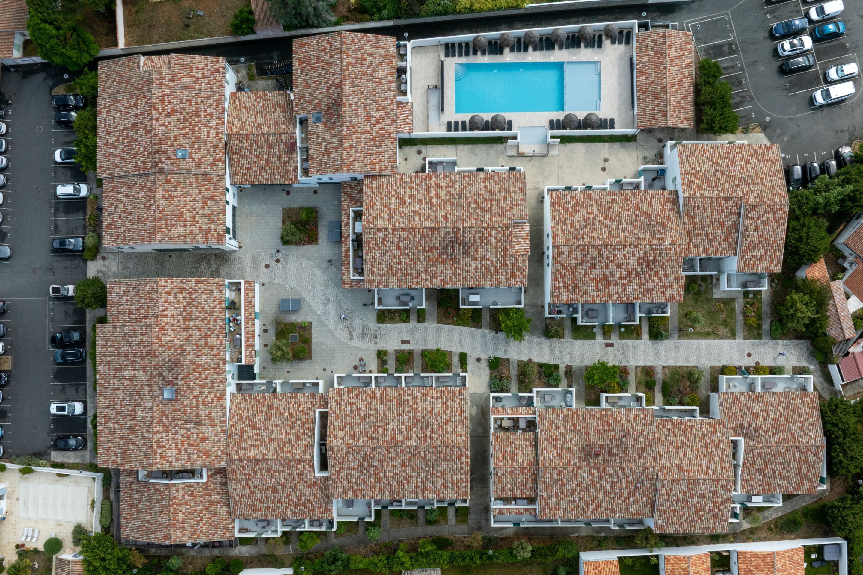 Vue aérienne d’un immeuble résidentiel doté de plusieurs unités abritées par des toits, d’une piscine et d’un espace de stationnement.