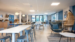 A modern dining area with white tables and chairs, a hanging chair, and large windows providing natural light. - Résidence Odalys Rêve d'lle (Rivedoux-Plage)