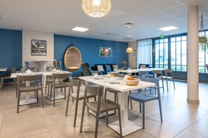 A modern dining area with tables and chairs, a hanging light fixture, and artwork on the walls. - Résidence Odalys Rêve d'lle (Rivedoux-Plage)