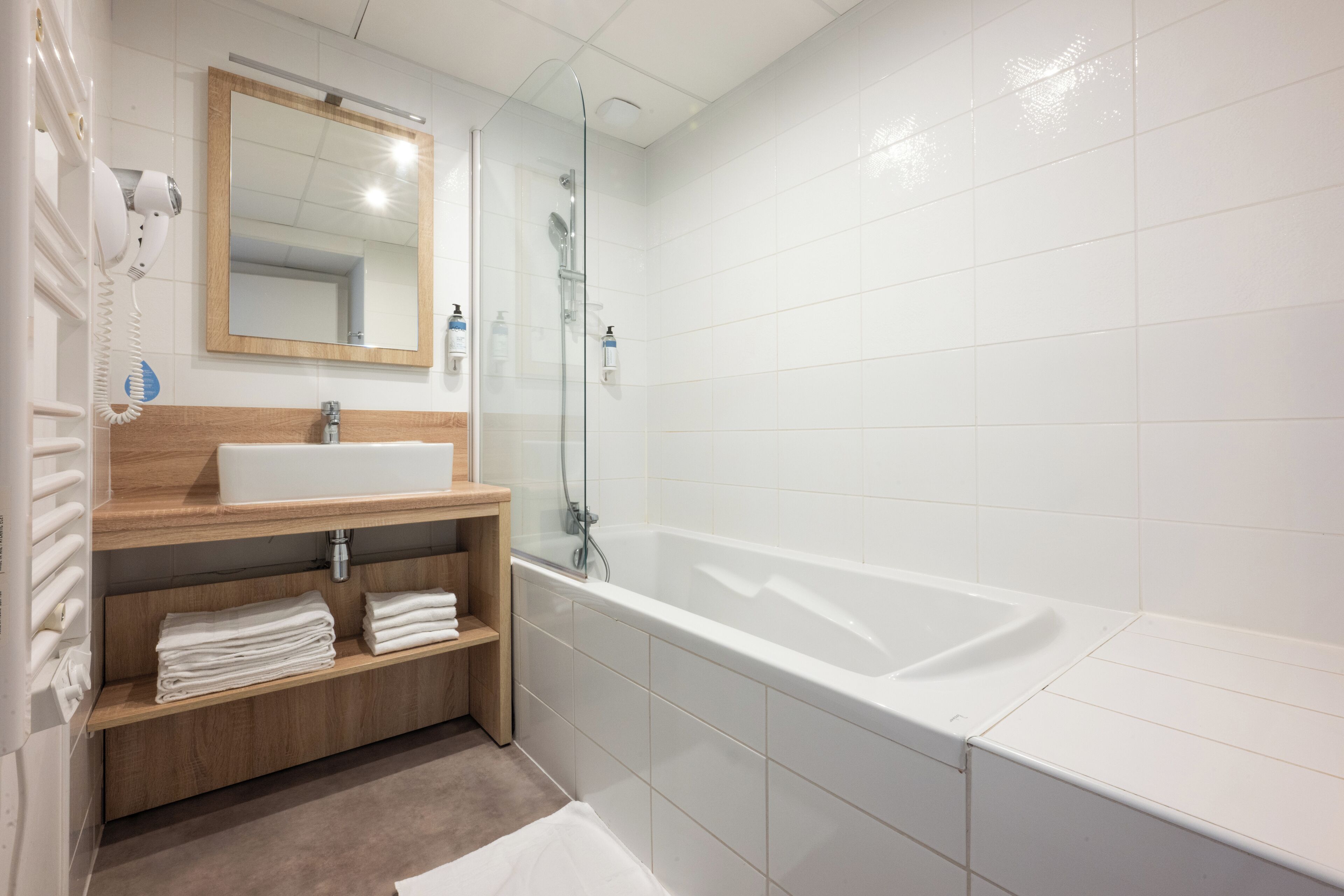 A modern bathroom with a large bathtub, a wooden vanity with a sink, and a glass shower enclosure.