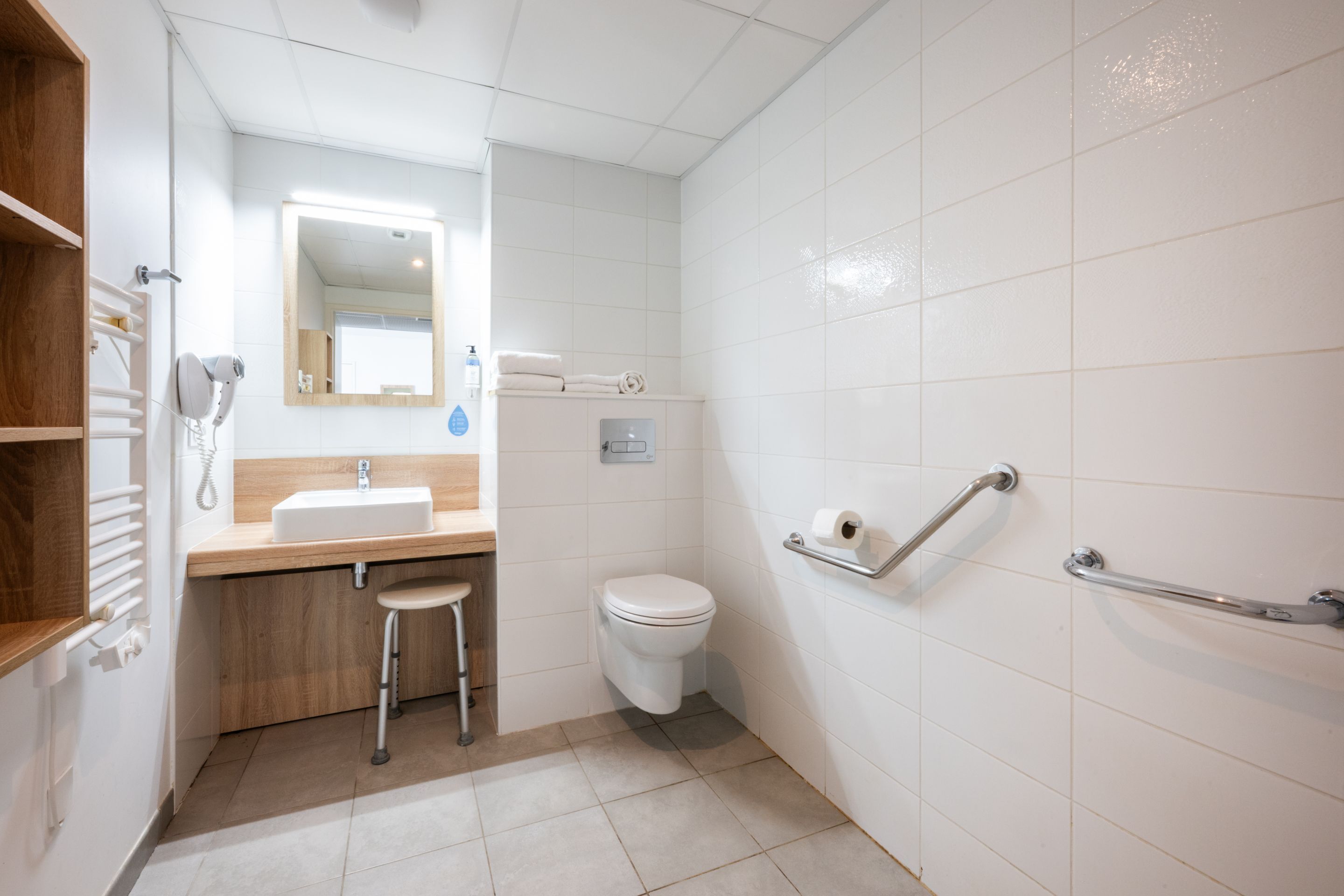 A modern bathroom with a sink, mirror, toilet, and grab bars.