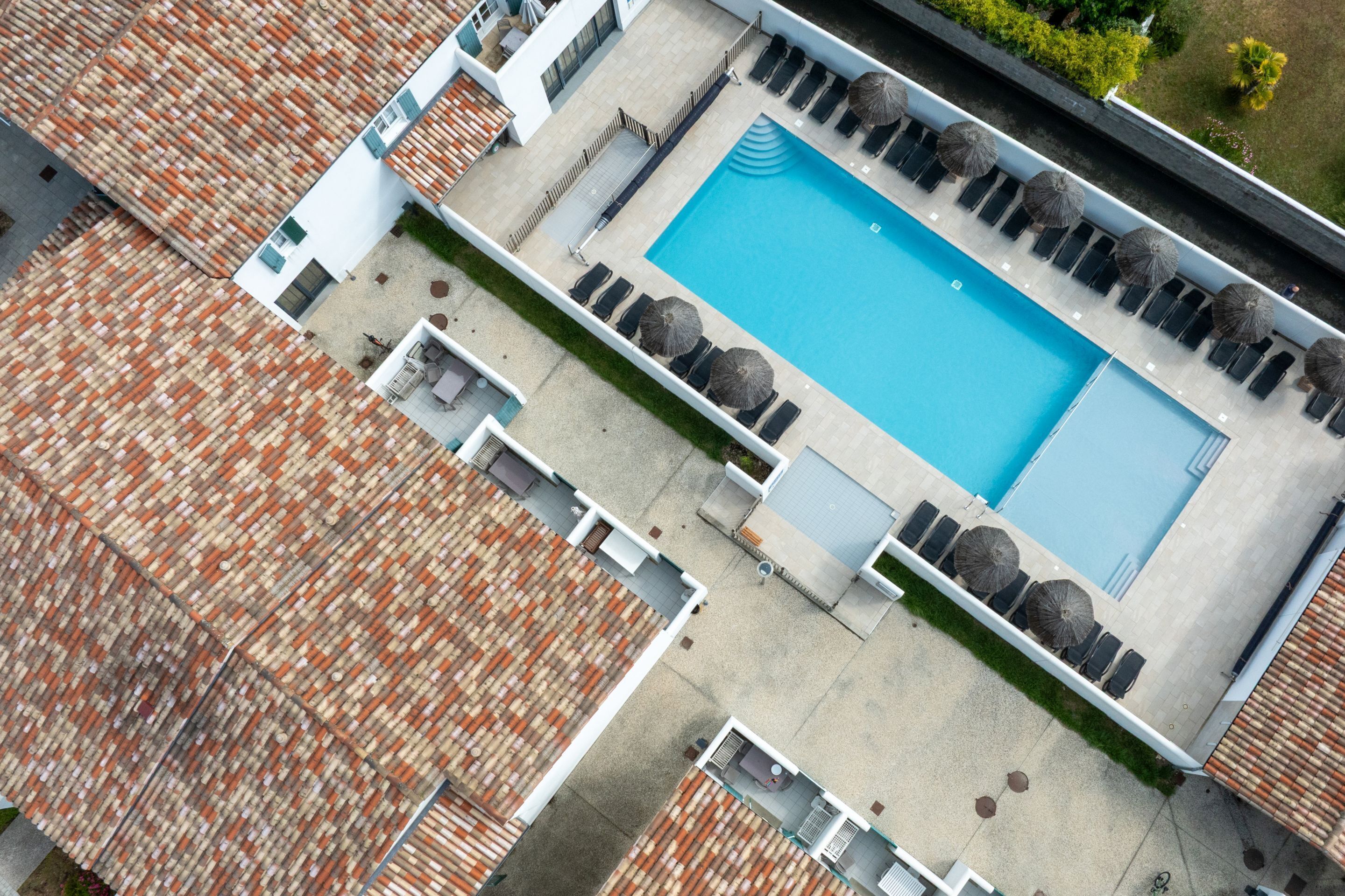 An aerial view of a hotel with a swimming pool, sun loungers, and umbrellas.
