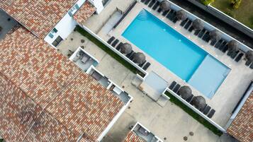 An aerial view of a hotel with a swimming pool, sun loungers, and umbrellas.