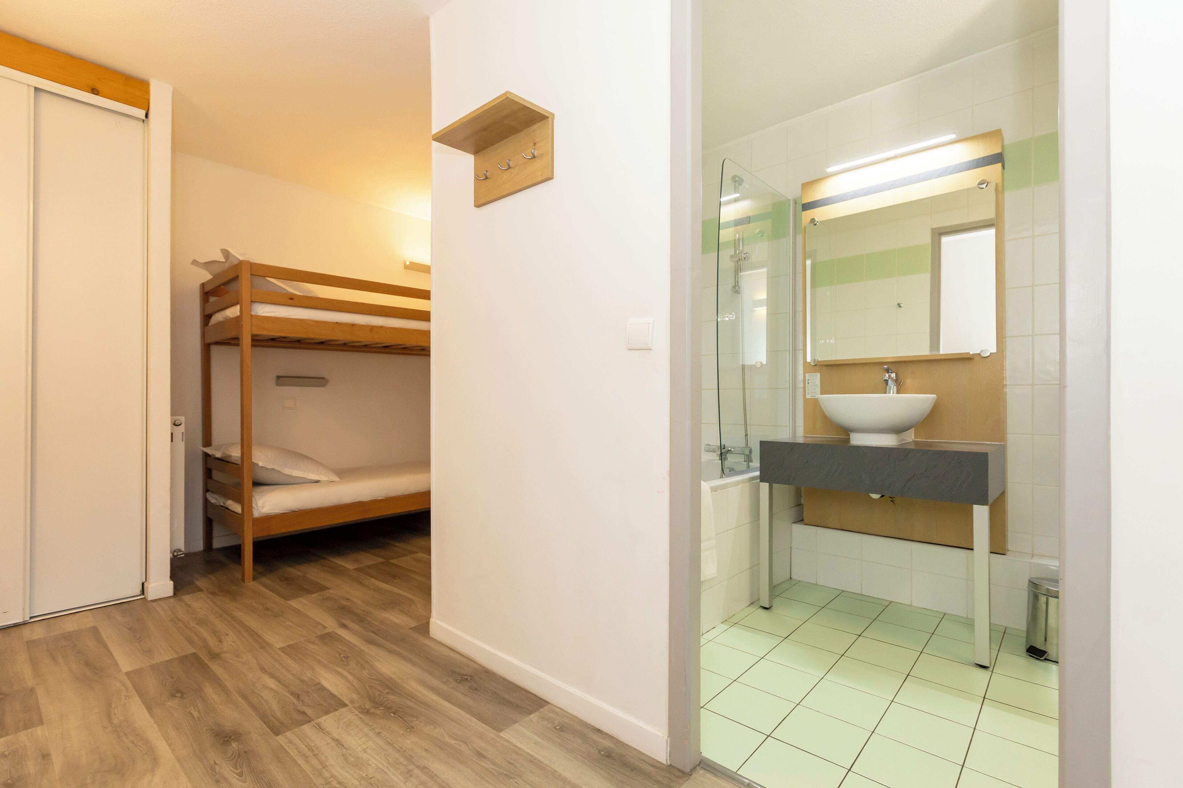 Una habitación con literas, baño con lavabo y espejo, y suelo de baldosas.