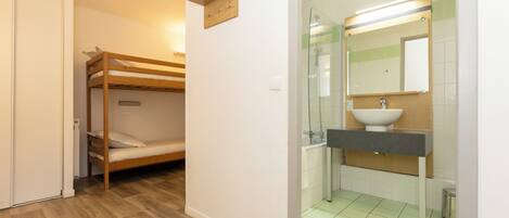 Una habitación con literas, baño con lavabo y espejo, y suelo de baldosas.
