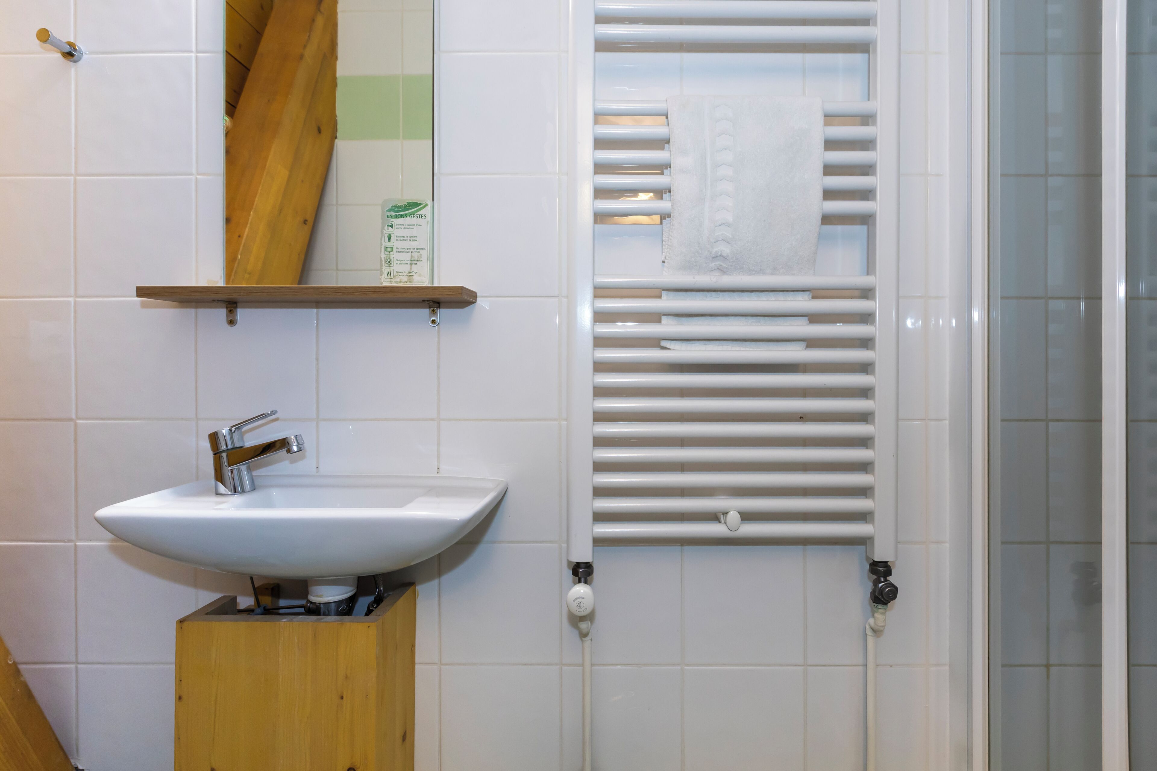 A bathroom with a white sink, a wooden shelf, a towel rack, and a shower area.