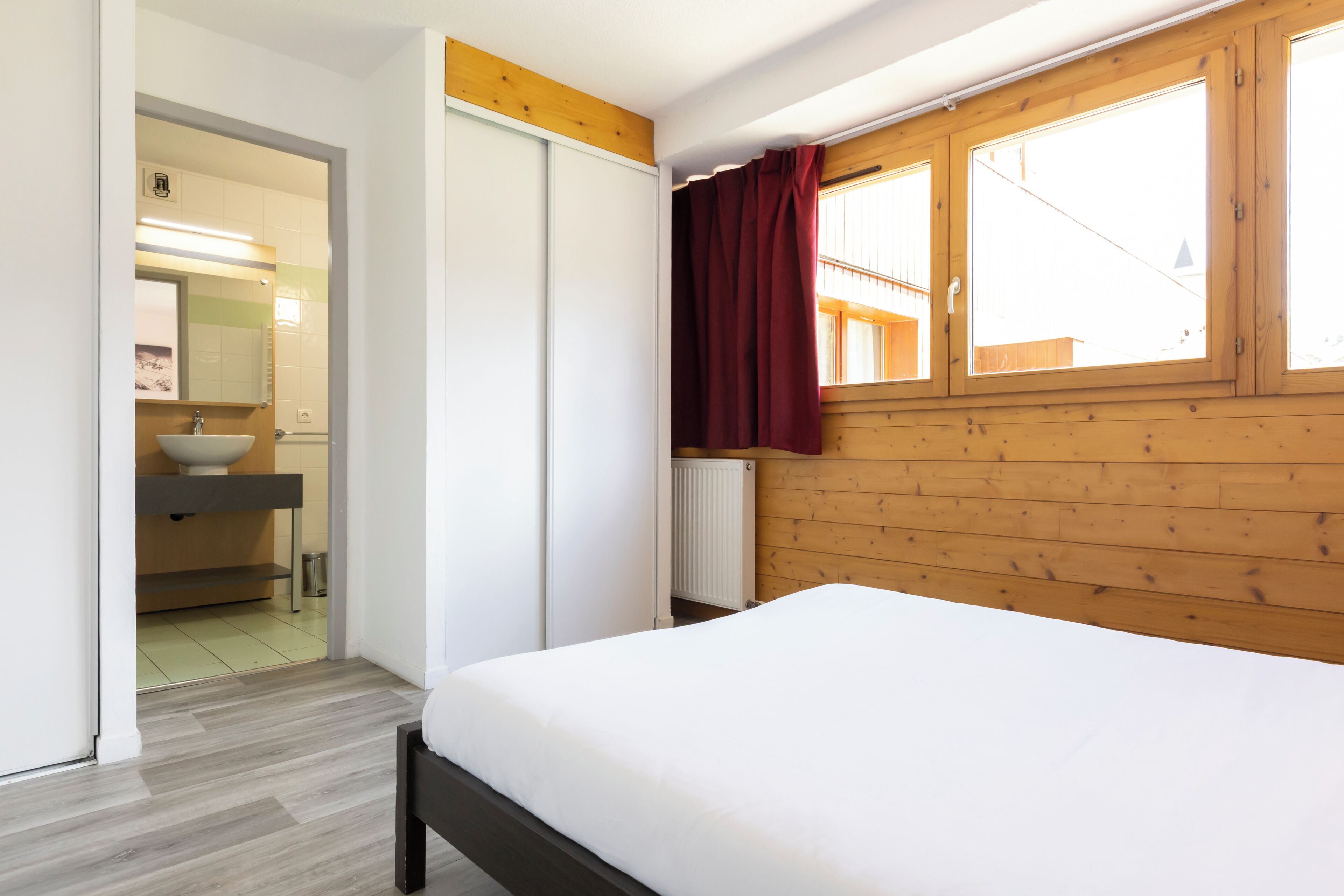 A bedroom with a bed, wooden walls, a window with a curtain, and a view of the outside.