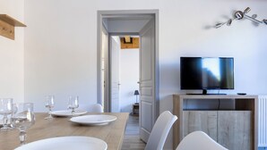 Ein moderner Essbereich mit einem Holztisch, weißen Tellern und Gläsern, einem Fernseher auf einem Holzschrank und einem weißen Stuhl.