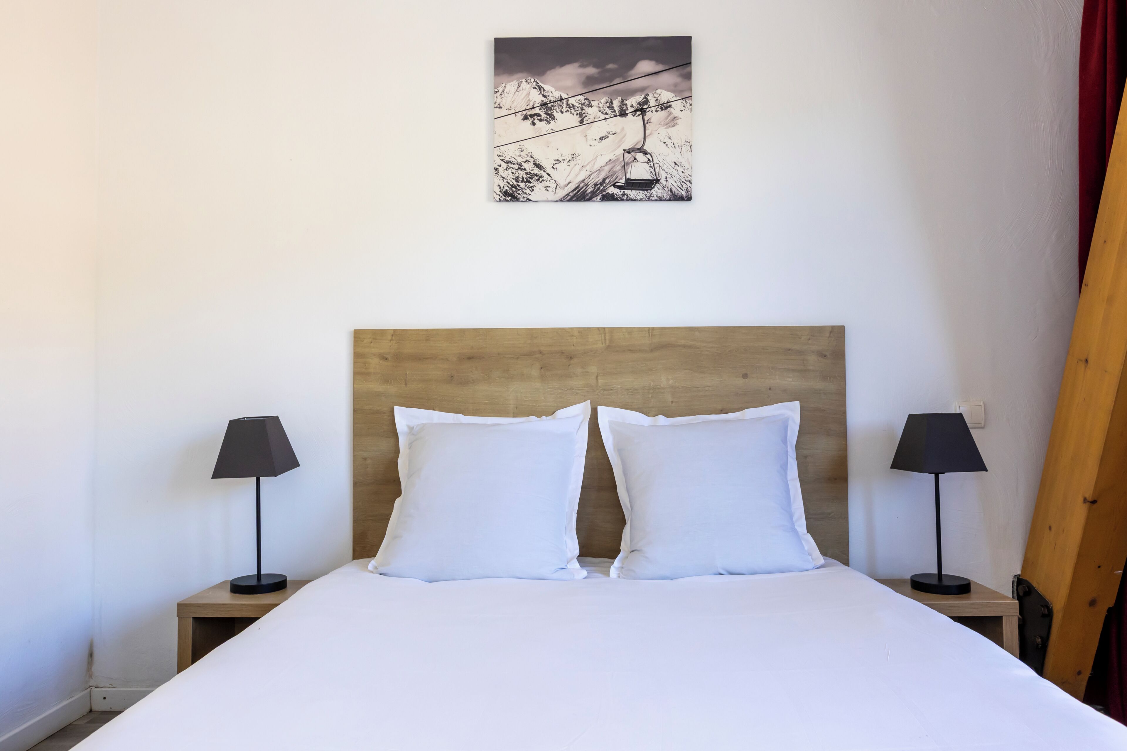 Una cama bien hecha con ropa blanca, dos mesitas de noche con lámparas, un cabecero de madera y un cuadro enmarcado en la pared.