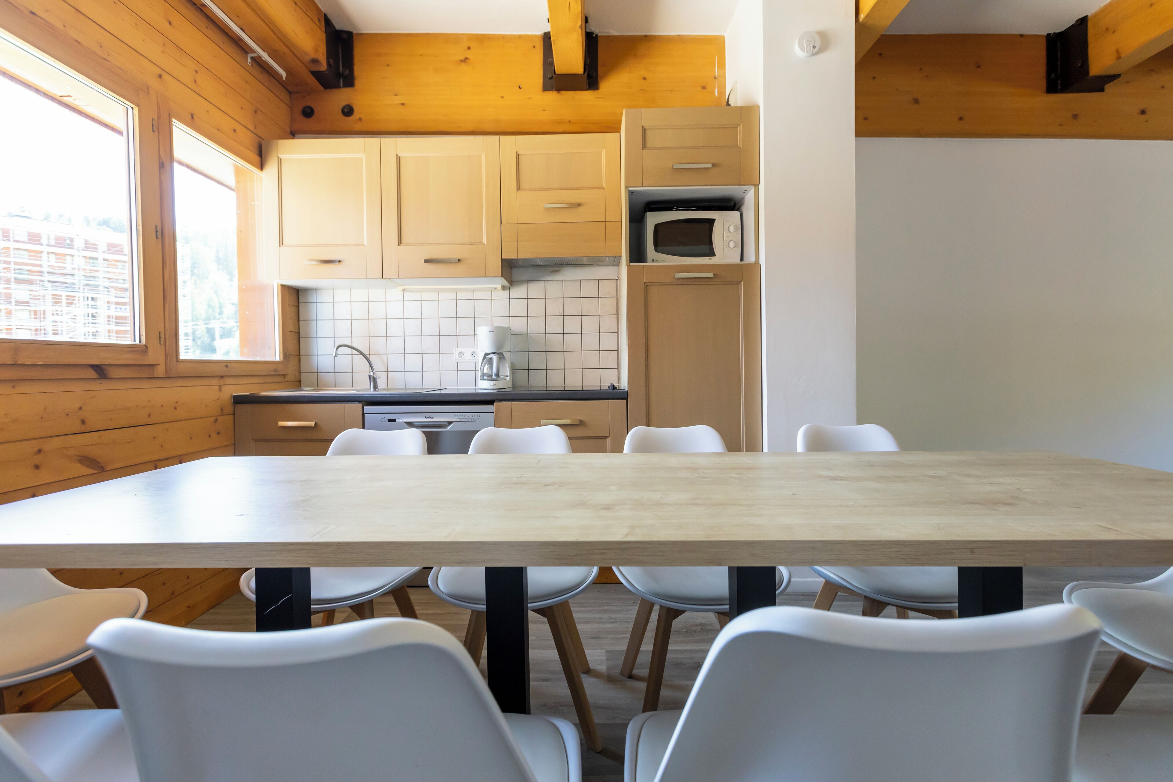 Una cocina moderna con armarios de madera, microondas y un comedor con mesa de madera y sillas blancas.