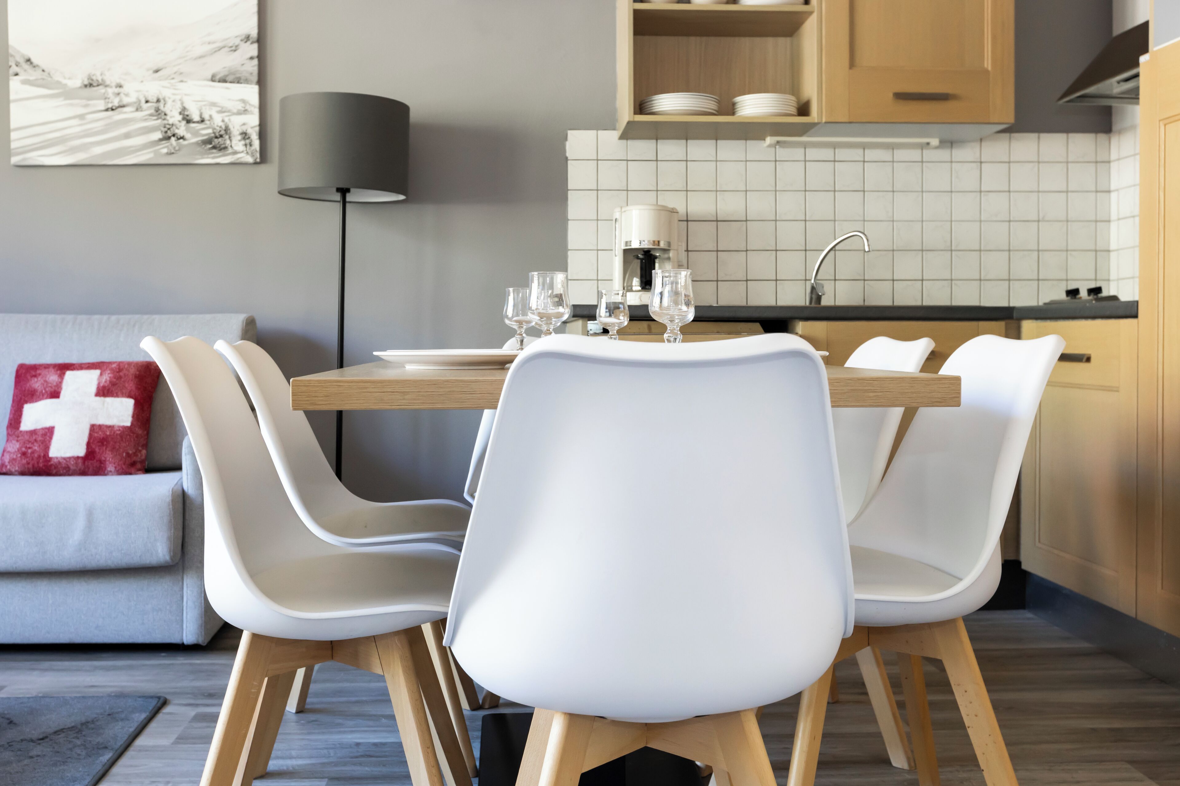 A modern kitchen with a dining table set for four, white chairs, a coffee machine, and a sink.