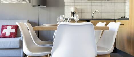 A modern kitchen with a dining table set for four, white chairs, a coffee machine, and a sink.
