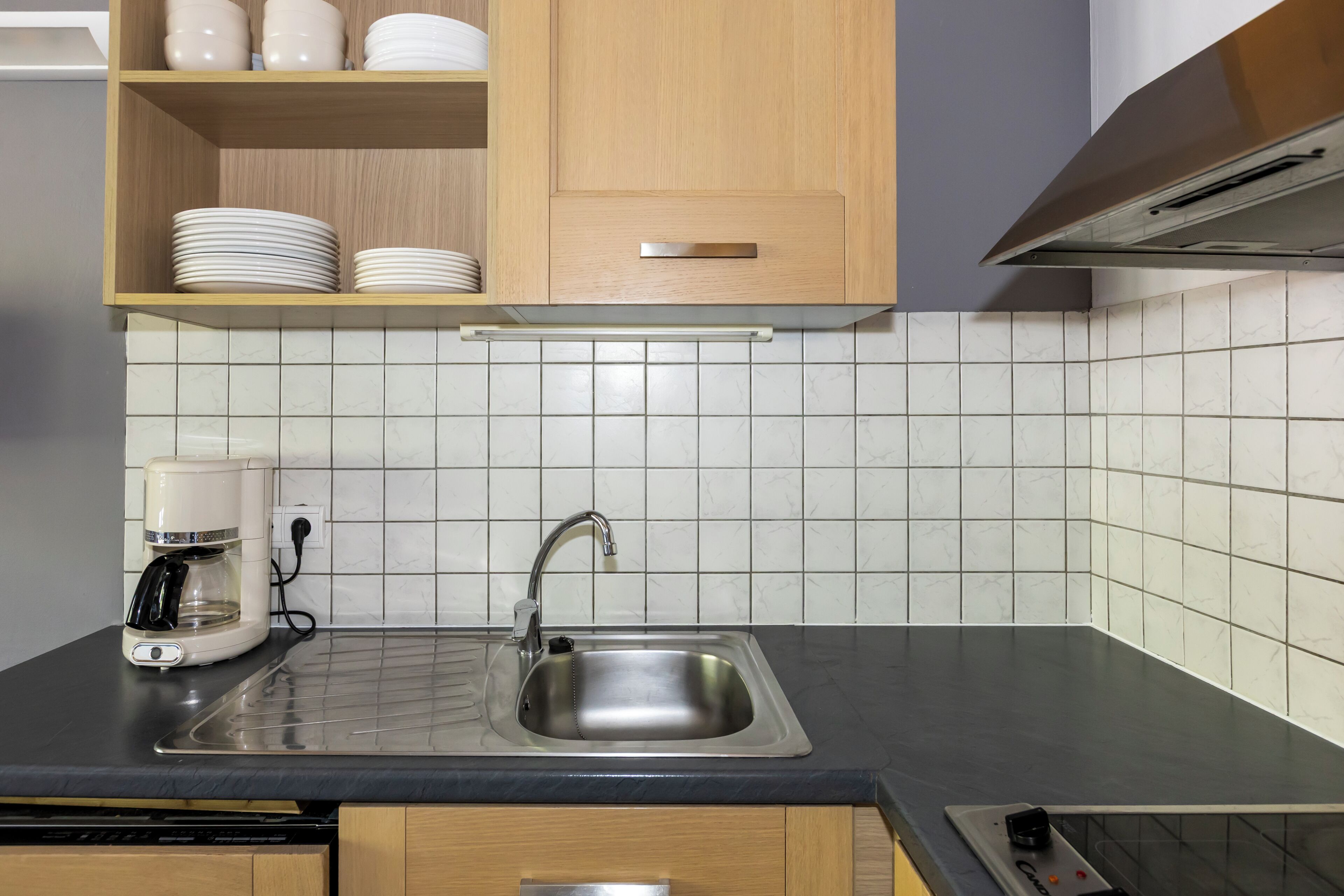 A kitchen with a sink, a coffee maker, and a cabinet with dishes.