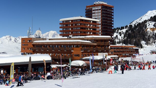 Ein Skigebiet mit einem großen Gebäude, das mehrere Balkone und eine Seilbahn im Hintergrund aufweist.