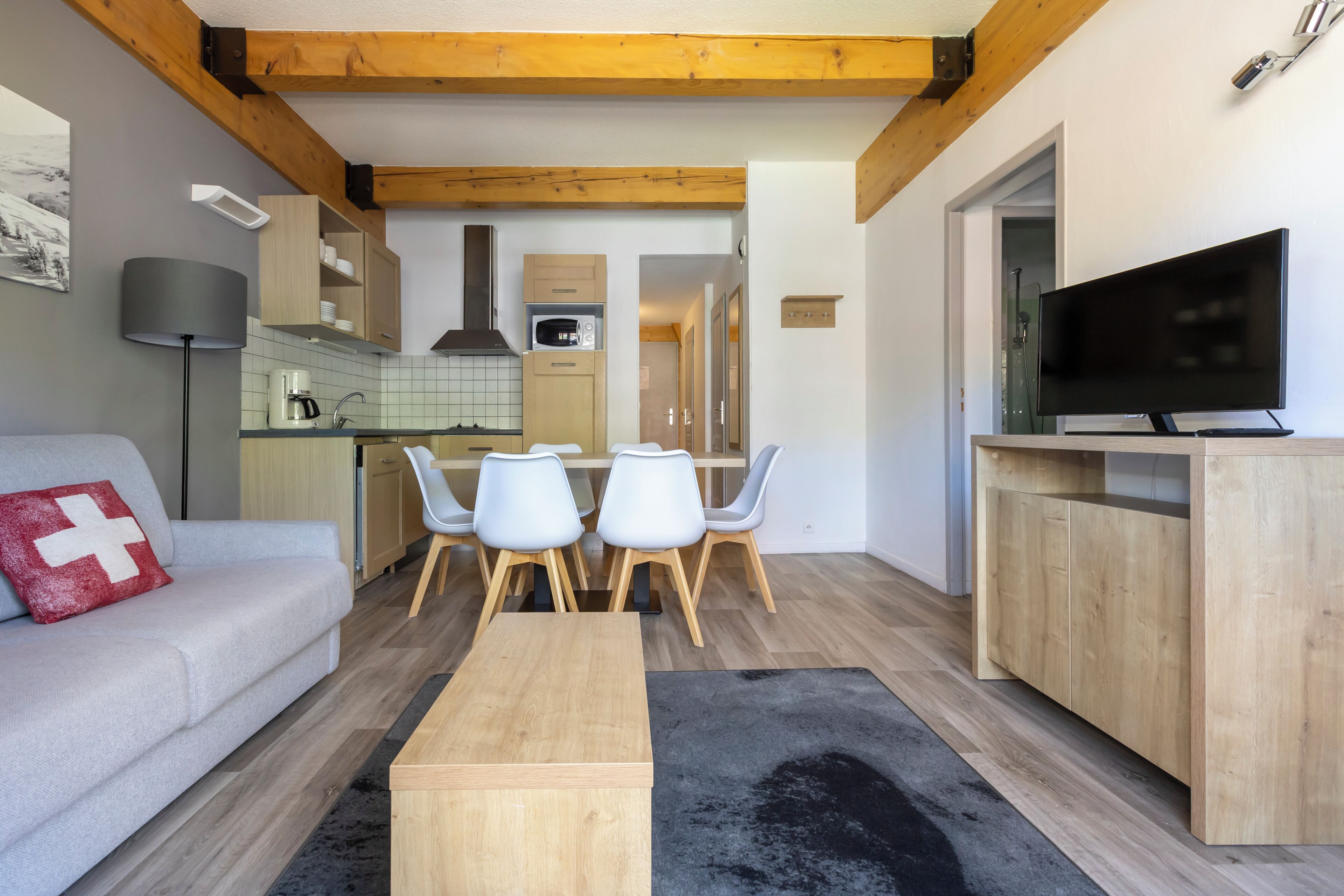 A modern living room with a sofa, a coffee table, a TV, and a dining area with chairs and a kitchen in the background.