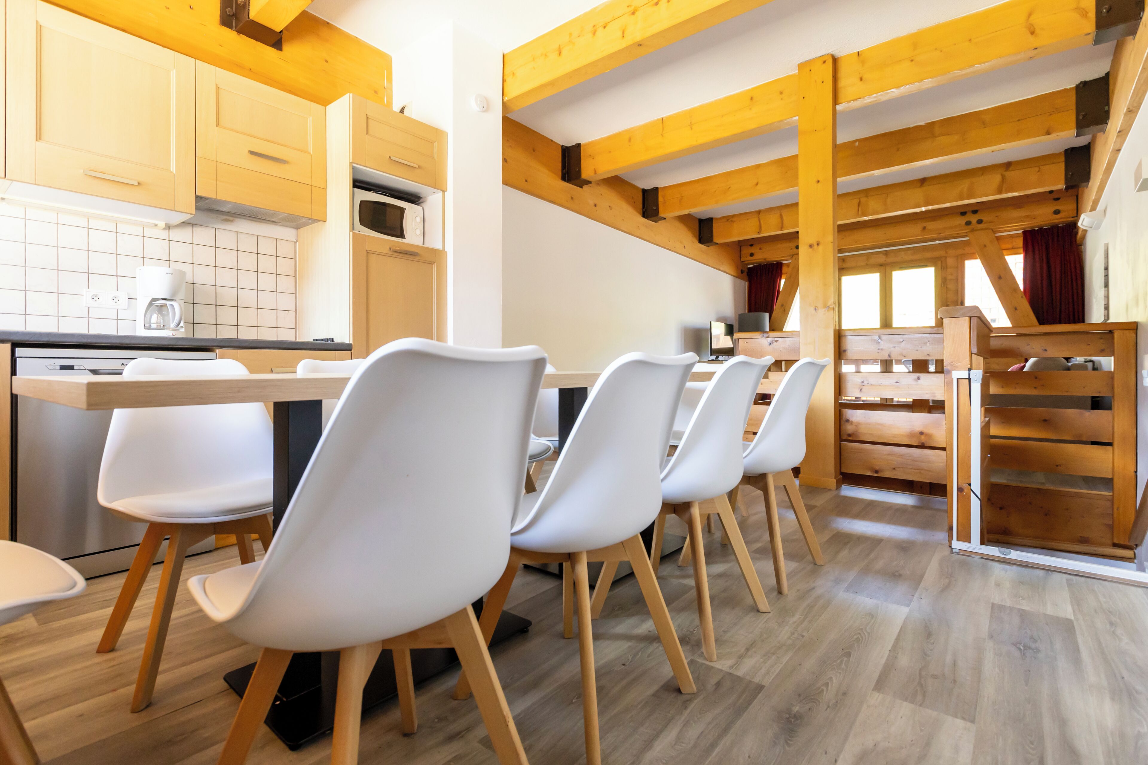 A modern kitchen with wooden beams, white chairs, and a dining table.