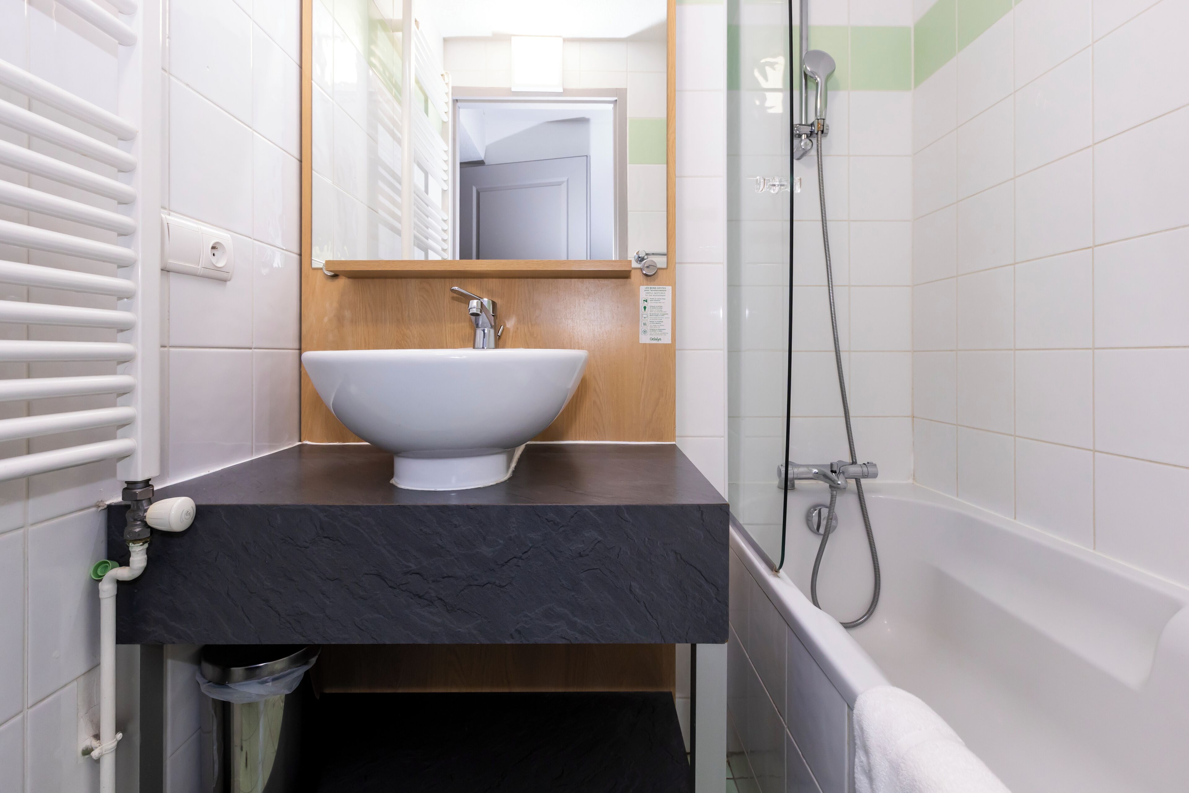 A bathroom with a white sink, black countertop, and a shower.