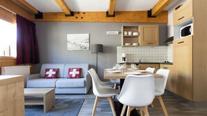 Eine moderne Küche mit Holzbalken, einem Essbereich mit weißen Stühlen, einer Couch mit rotem Kissen und einer Kücheninsel.