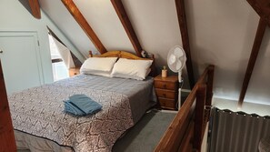 Ein Schlafzimmer mit einem Bett, Nachttischen, einem Ventilator und einem Fenster.