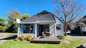 Une petite maison de plain-pied, avec un toit recouvert de bardeaux sombres, une antenne parabolique et une véranda à l’avant, équipée d’une table et de chaises.