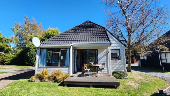 Ein kleines, eingeschossiges Haus mit dunklem Schindeldach, einer Satellitenschüssel und einer Veranda mit Tisch und Stühlen.