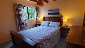 Une chambre à coucher avec un lit, des tables de chevet, une fenêtre avec des rideaux, une lampe et un tableau au mur.