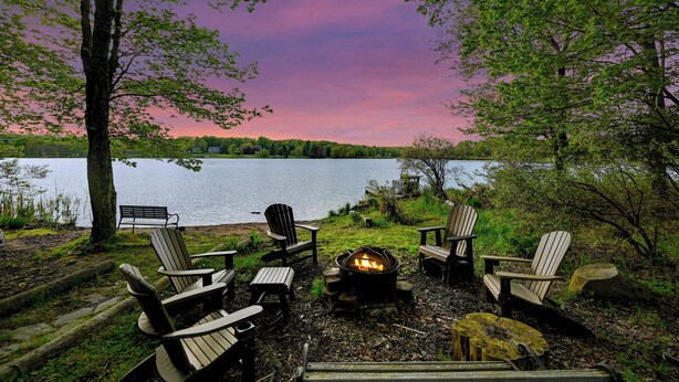 A lakeside seating area with Adirondack chairs and a fire pit.