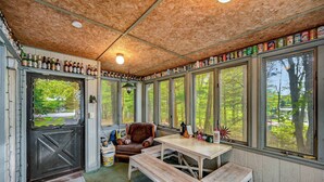 A rustic cabin with a wooden ceiling, a dining table, benches, and a leather chair.