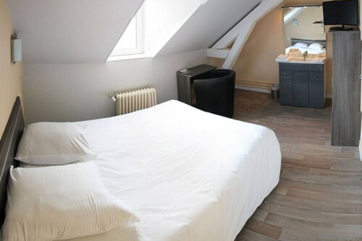 A bedroom with a bed, a radiator, a trash bin, a TV, and a small kitchenette area.