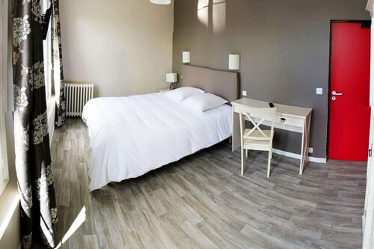 A bedroom with a bed, bedside table, lamp, and a red door.